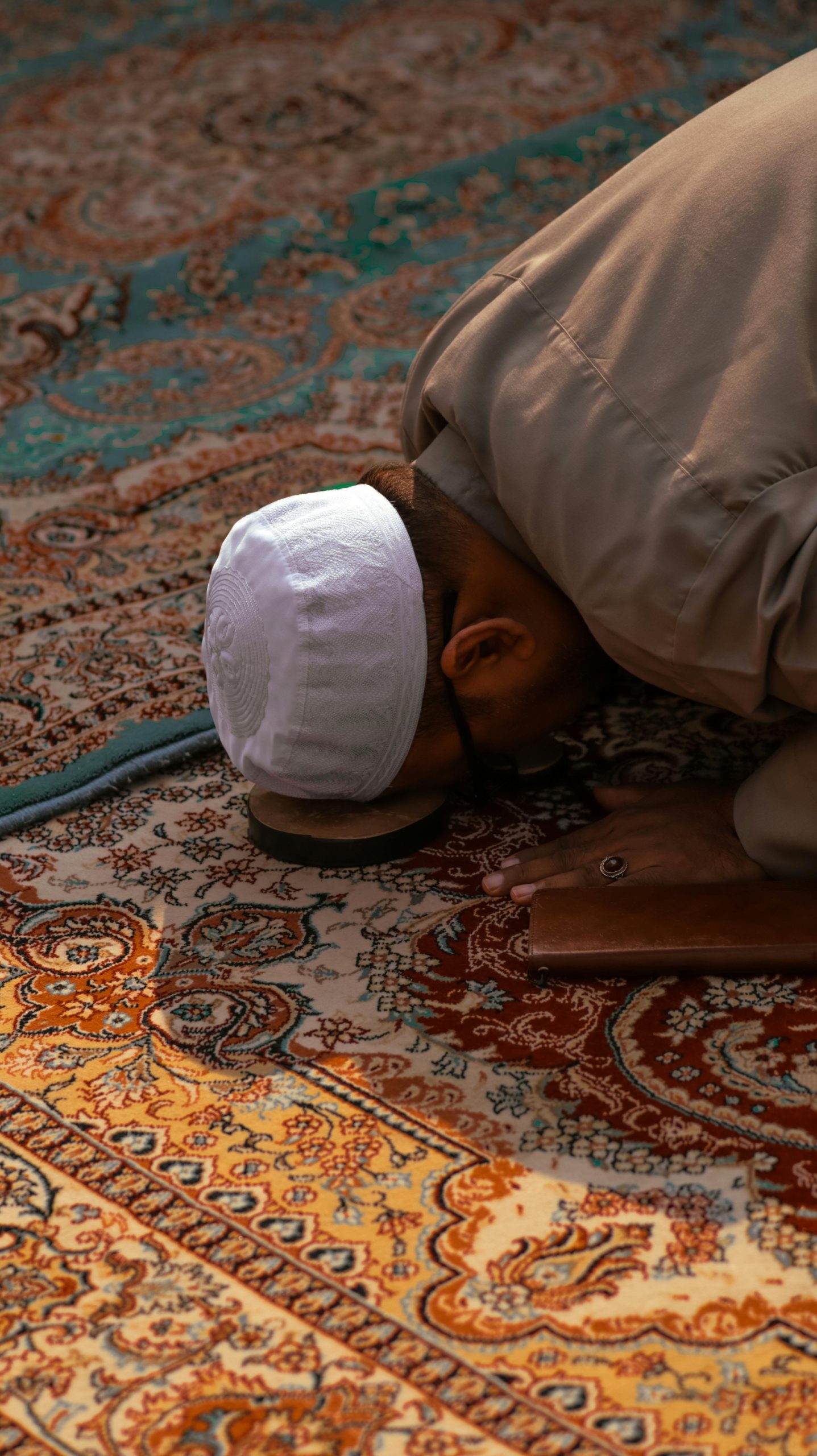 Man in traditional attire praying on a beautiful Persian carpet indoors, showcasing Islamic spirituality.